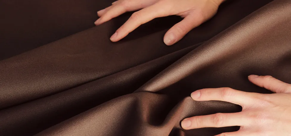 Hands smoothing a sheet of brown non-woven fabric